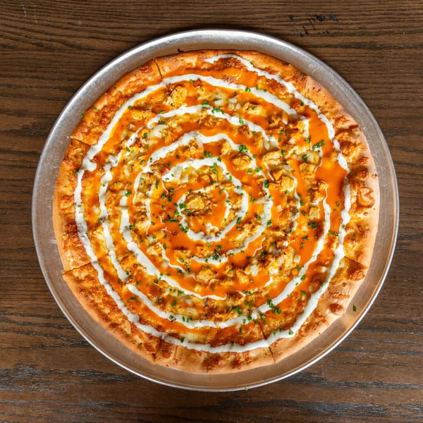 A buffalo chicken pizza with ranch and chives, on a metal pan, on a wooden table.