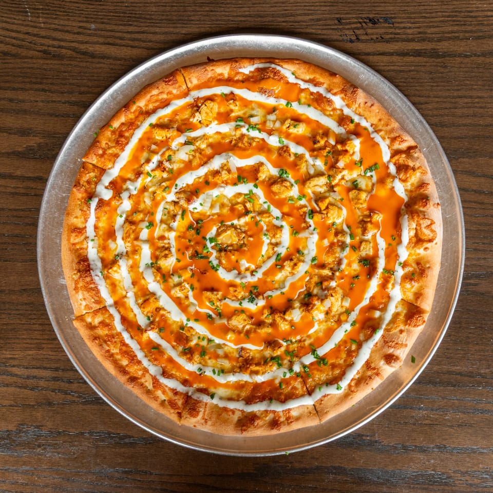 A buffalo chicken pizza with ranch and chives, on a metal pan, on a wooden table.