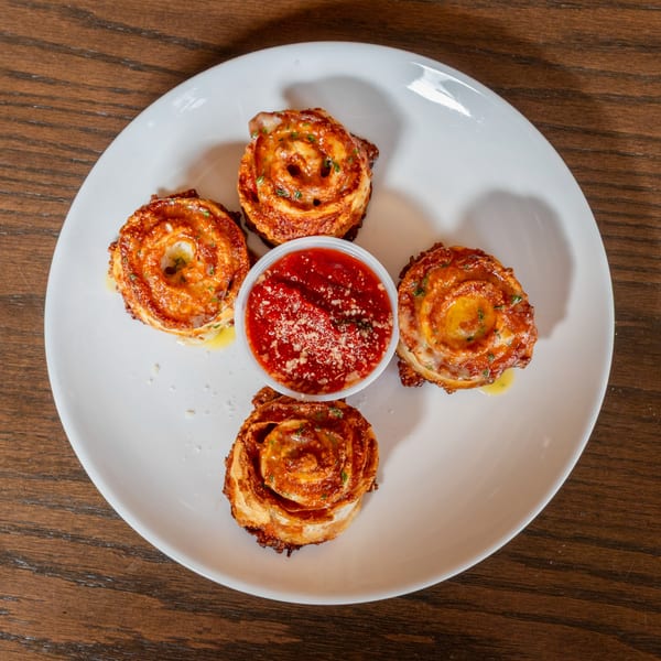 Four golden-brown pizza rolls with melted cheese and herbs, surrounding a cup of marinara sauce.