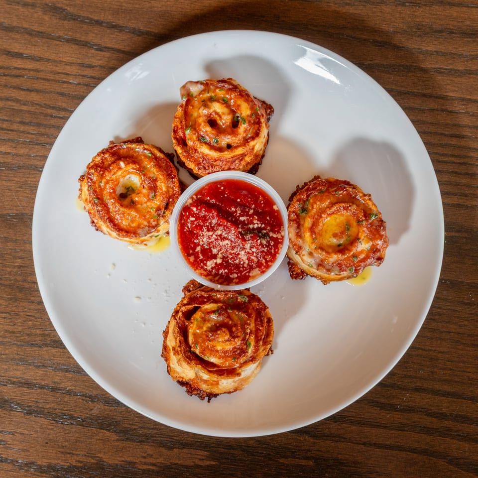 Four golden-brown pizza rolls with melted cheese and herbs, surrounding a cup of marinara sauce.
