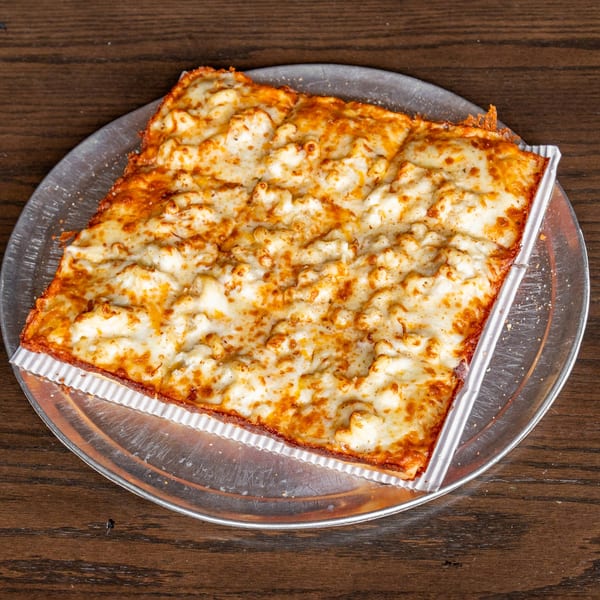 Square mac and cheese pizza with a golden crust on a metal pan, on a wooden table.