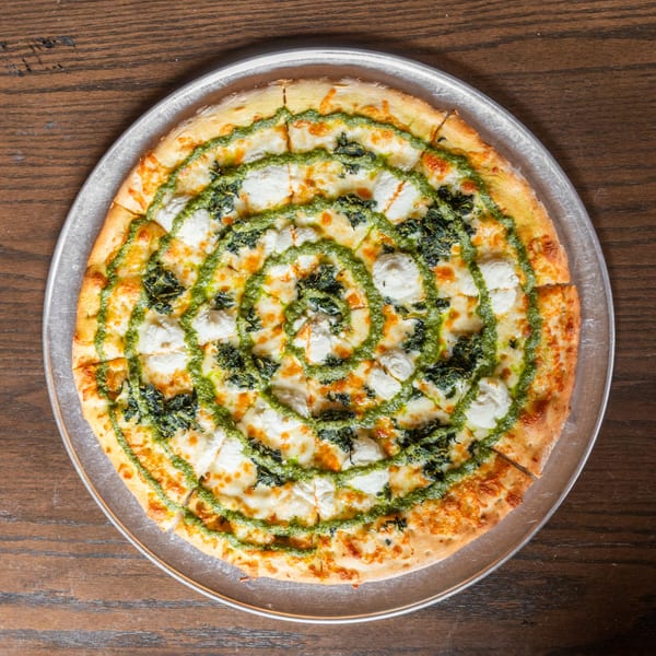 Overhead view of a sliced pizza with pesto, ricotta, and spinach on a metal tray.