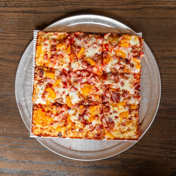 Square Detroit-style pizza with ham, bacon, and pineapple on a metal tray.