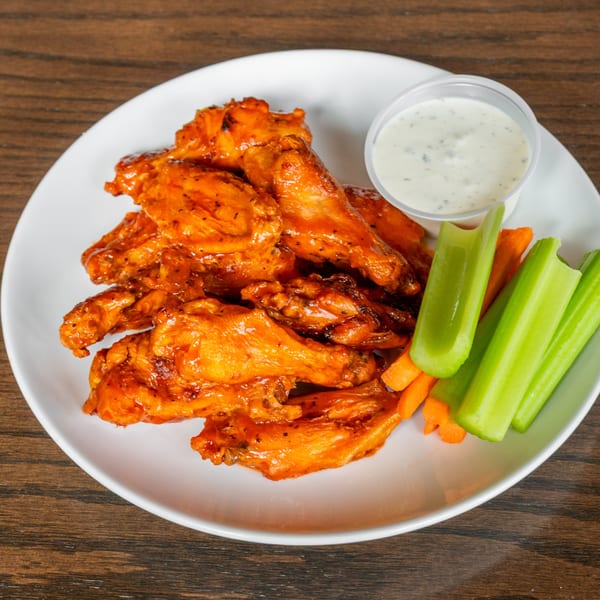 Spicy buffalo chicken wings with ranch dressing, celery, and carrot sticks on a white plate.